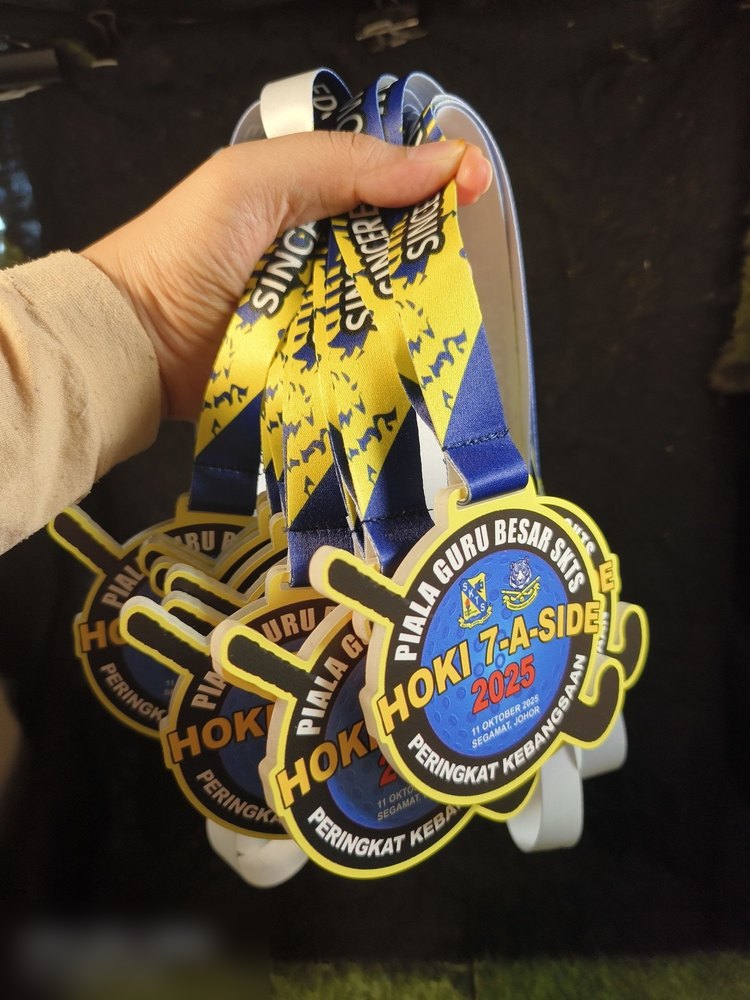 Medal Hoki 7-A-Side SKTS 2025 dalam kuantiti — beberapa keping dengan lanyard kuning-biru bercetak 'SINCERE'. Tunjuk order untuk kejohanan penuh.