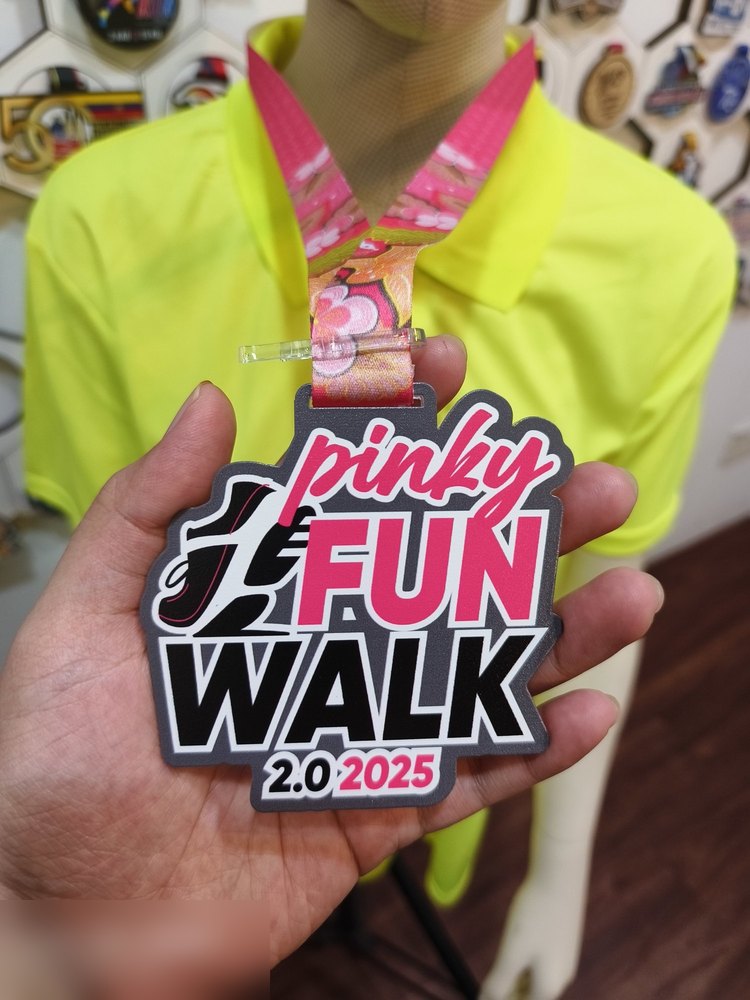 Medal Pinky Fun Walk 2.0 2025. Bentuk custom, latar kelabu gelap dgn teks 'pinky' dlm tulisan sambung MERAH JAMBU terang dan 'FUN WALK' hitam-putih tebal. Lanyard merah jambu berbunga. Design bersih d