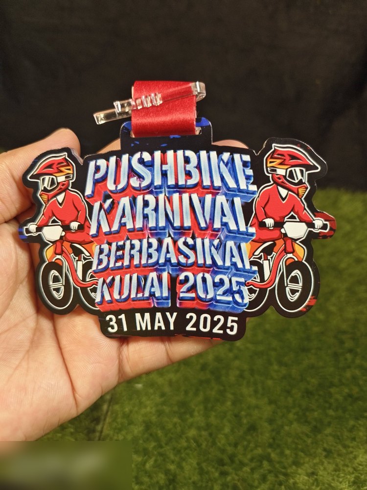 Medal Pushbike Karnival Berbasikal Kulai 2025 (31 Mei 2025). Bentuk custom dgn DUA watak kartun penunggang berbaju merah di kiri dan kanan, teks graffiti biru-merah bertindan. Reben merah. Sesuai karn