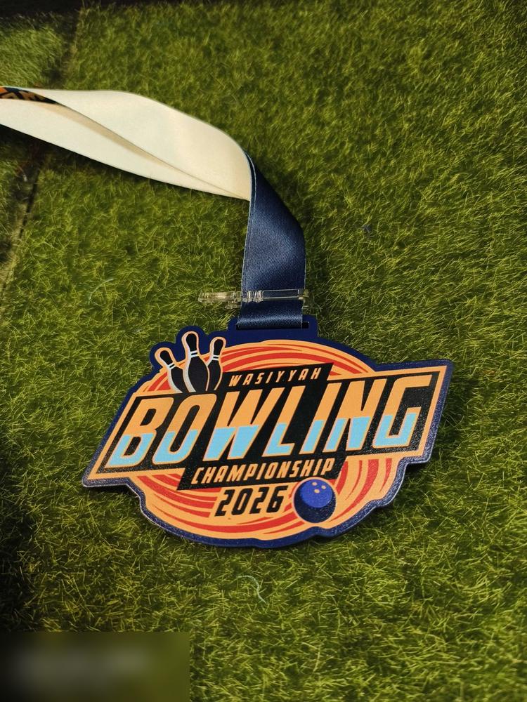 Medal Wasiyyah Bowling Championship 2026. Bentuk custom mengikut teks 'BOWLING' dengan pin dan bola bowling. Warna biru navy, oren dan biru muda dengan garisan lorong bowling. Reben biru gelap dengan